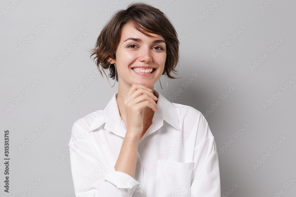 Charming young business woman in white shirt posing isolated on grey wall background in studio. Achievement career wealth business concept. Mock up copy space. Put hand prop up on chin looking camera. Charming young business woman in white shirt posing isolated on grey wall background in studio. Achievement career wealth business concept. Mock up copy space. Put hand prop up on chin looking camera.