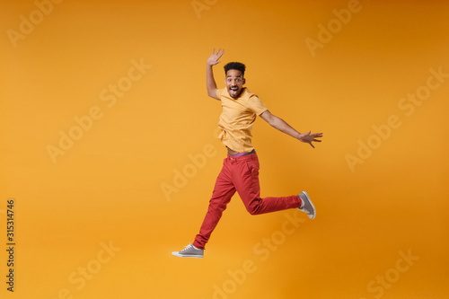 Excited young african american guy in bright casual clothes posing isolated on yellow orange background studio portrait. People emotions lifestyle concept. Mock up copy space. Jumping spreading hands.