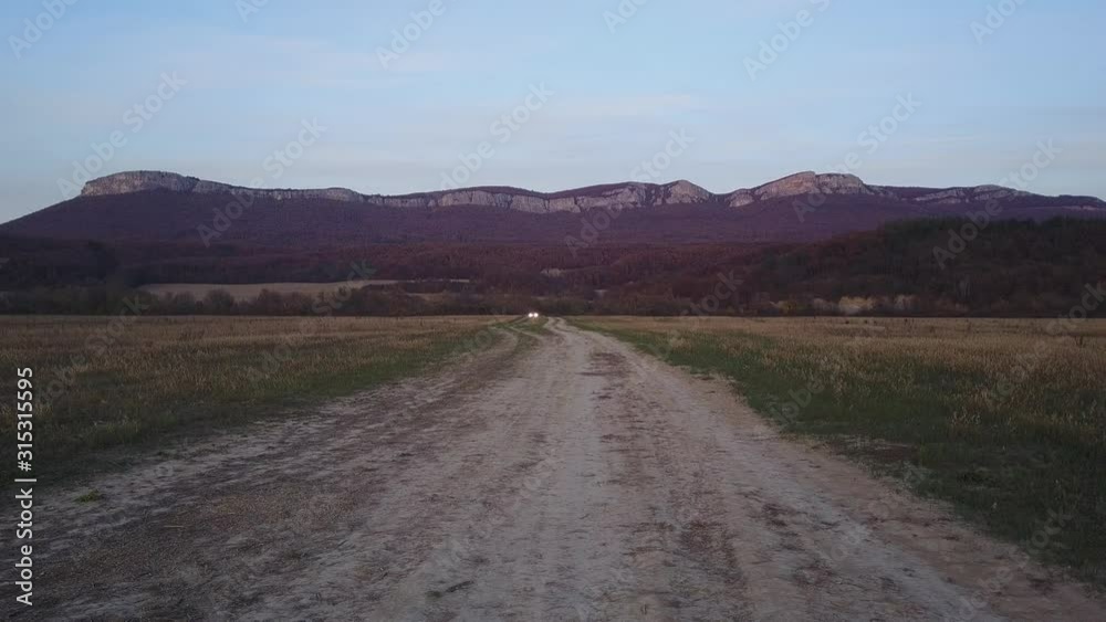 Aerial towards fast white suv car on dirt path with mountain in the background Aerial towards fast white suv car on dirt path with mountain in the background