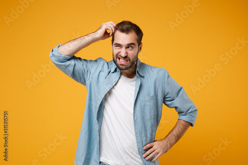 Preoccupied young bearded man in casual blue shirt posing isolated on yellow orange background studio portrait. People emotions lifestyle concept. Mock up copy space. Putting hand on head, looking up.