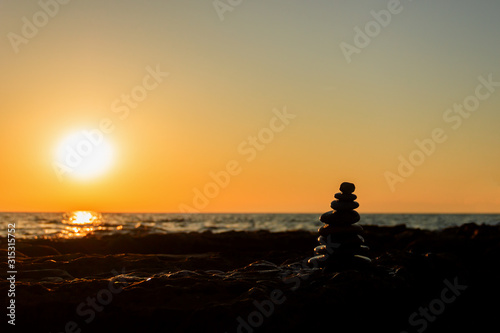 Silhouette of a pyramid of stones for meditation, lying on the sea coast at sunset, in the contoured light of the sun. Low key photography