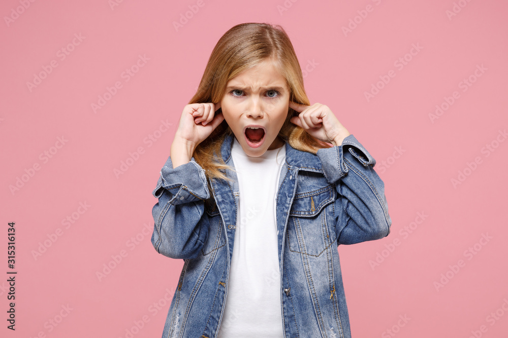 Shocked little kid girl 12-13 years old in denim jacket isolated on pastel pink background in studio. Childhood lifestyle concept. Mock up copy space. Keeping mouth open, covering ears with fingers. Shocked little kid girl 12-13 years old in denim jacket isolated on pastel pink background in studio. Childhood lifestyle concept. Mock up copy space. Keeping mouth open, covering ears with fingers.