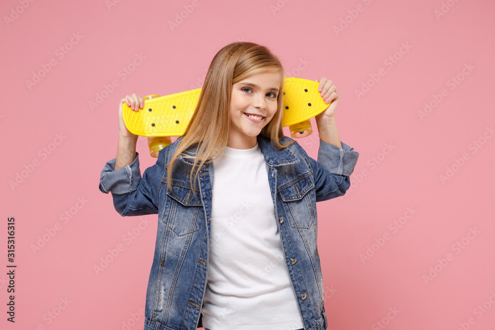 Smiling little blonde kid girl 12-13 years old in denim jacket posing isolated on pastel pink background children portrait. Childhood lifestyle concept. Mock up copy space. Hold yellow skateboard. - obrazy, fototapety, plakaty 