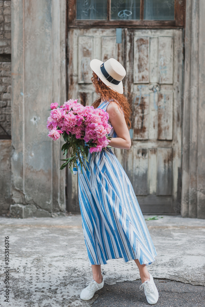 unrecognizable girl in hat with  peonies bouquet on the vintage wall background. No face