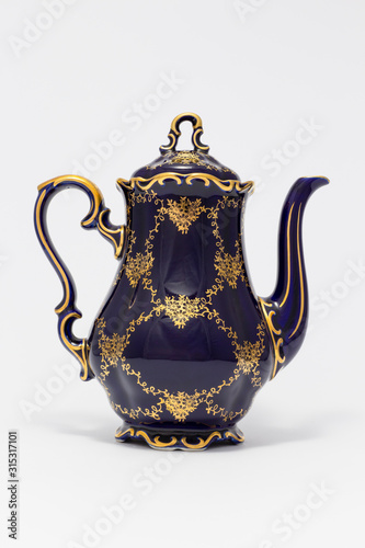 Closeup of a beautiful cobalt blue colored vintage porcelain teapot with golden floral pattern on white background
