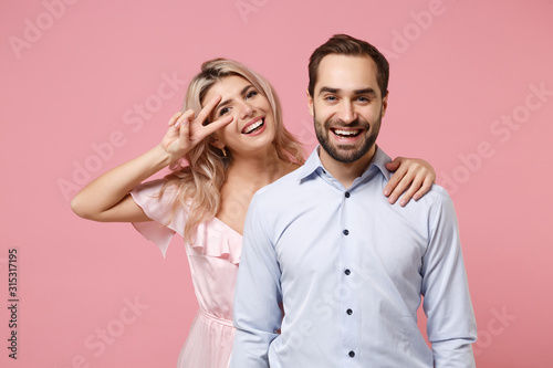 Cheerful young couple two guy girl in party outfit celebrating posing isolated on pastel pink background. People lifestyle Valentine's Day Women's Day birthday holiday concept. Showing victory sign.