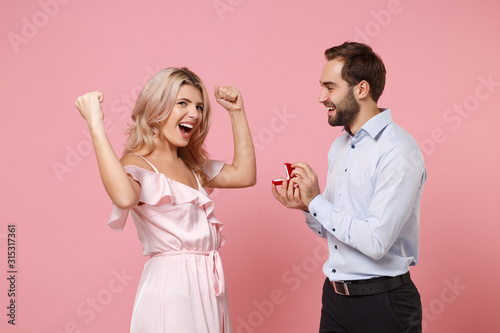 Couple two guy girl in party outfit celebrating posing isolated on pastel pink background. Valentine's Day Women's Day birthday holiday concept. Hold gift box with proposal ring doing winner gesture.