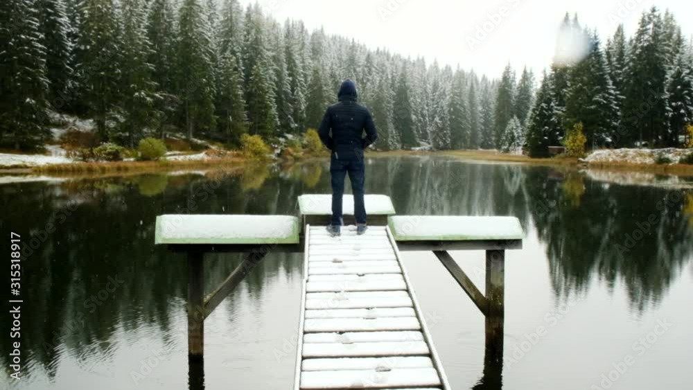 Beautiful forest lake in winter. Traveler on a wooden snow bridge looks at the lake Beautiful forest lake in winter. Traveler on a wooden snow bridge looks at the lake