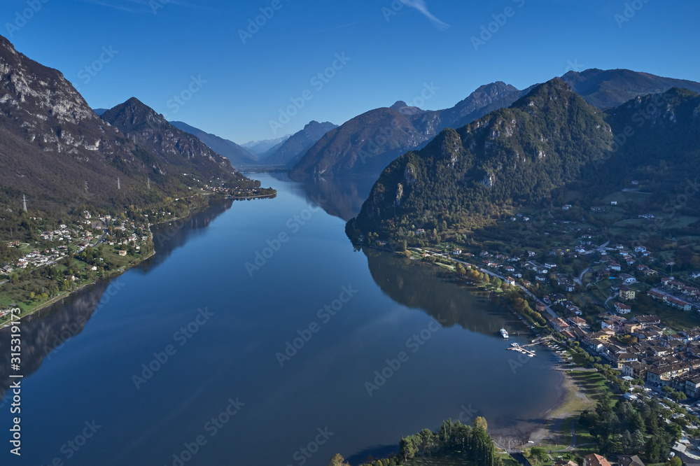Panoramic view of the mountains and Lake Idro. Autumn season, the reflection in the water of the mountains, trees, blue sky. Aerial view, drone photo