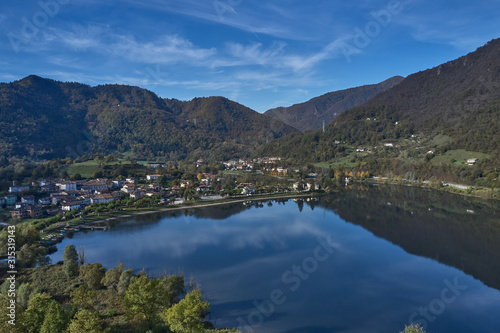 Panoramic view of the mountains and Lake Idro. Autumn season, the reflection in the water of the mountains, trees, blue sky. Aerial view, drone photo