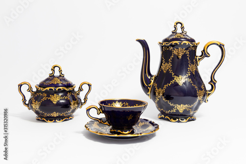 Closeup of a beautiful cobalt blue colored vintage porcelain tea set with golden floral pattern on white background. The set includes a tea pot, a sugar bowl and a tea cup.