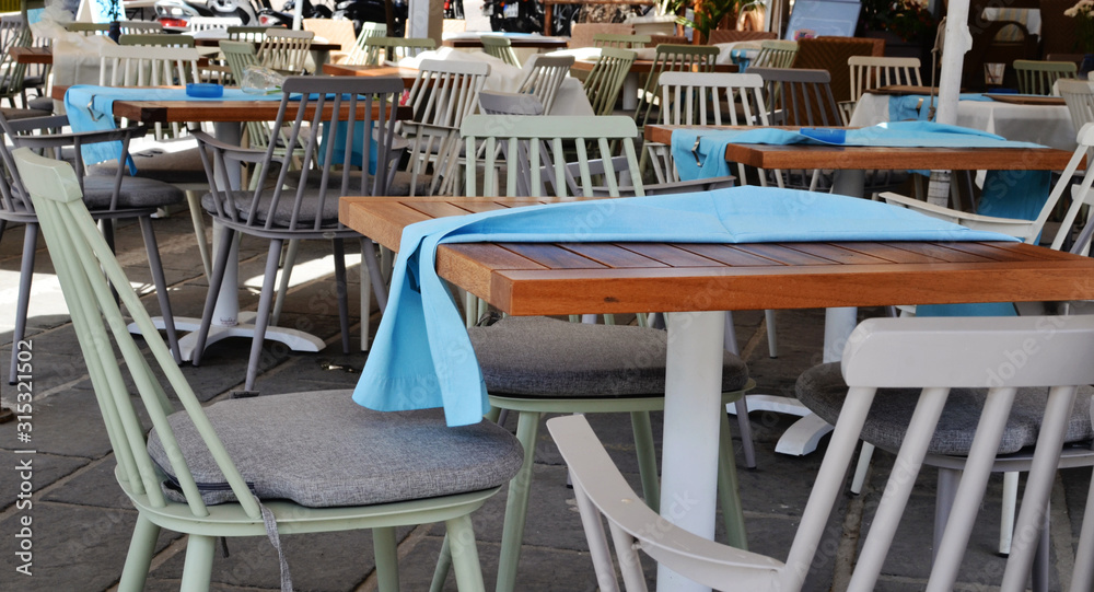 Stylish wooden chairs and table with blue tablecloth in garden restaurant. Patio in cafe with white furniture. Outdoors. Banner.