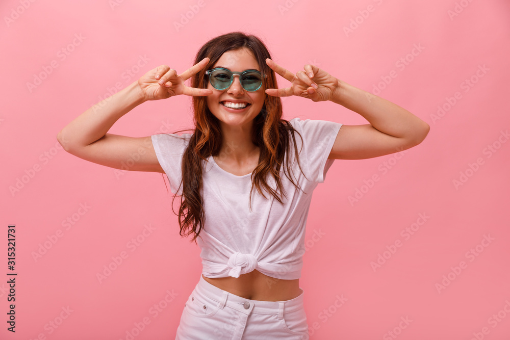 Portrait of a happy cheerful girl in summer hat showing peace gesture with two hands isolated over pink background.Indoor portrait of European girl isolated on gray background in casual clothes with o