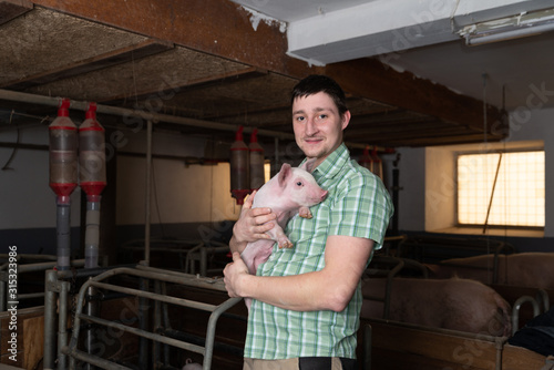 junger Bauer hält kleines Ferkel in der Hand, Schwein