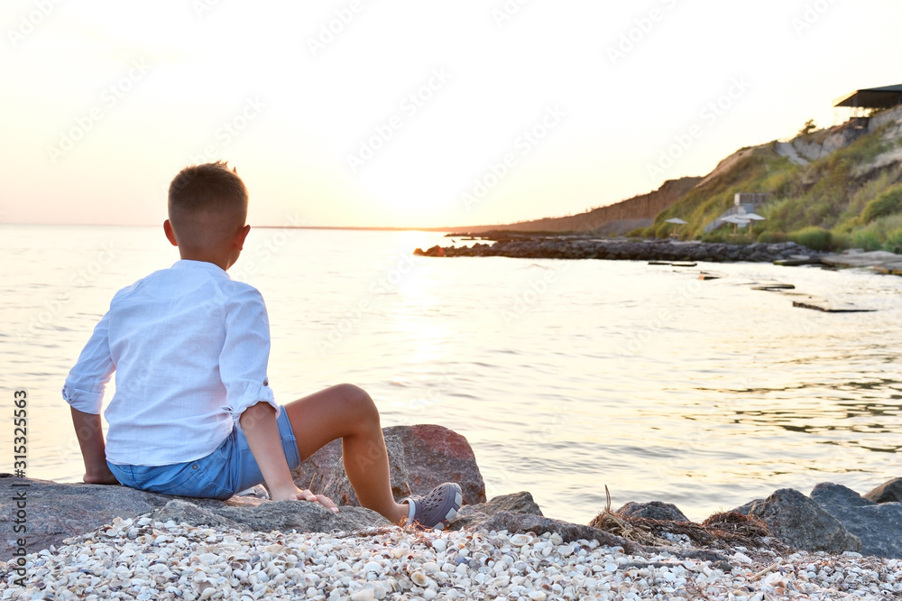 Boy sitting on the seashore watching the sunset