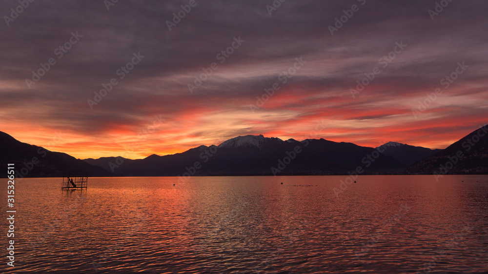 Favoloso tramonto sul lago, con panoramica del cielo con nuvole gialle, arancioni e rosse e bagliori dorati