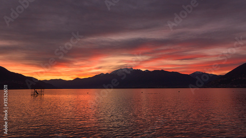 Favoloso tramonto sul lago, con panoramica del cielo con nuvole gialle, arancioni e rosse e bagliori dorati