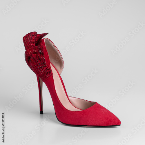 Womens red suede high heel shoes with decorative rhinestone bow on the heel. Close-up side view on a white background