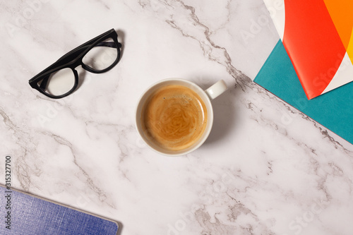 White cup of coffee on marble background with colorful notebooks and classical glasses 