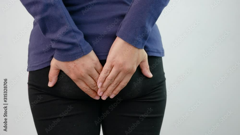 Close up of woman hands touch at her buttom, suffering from hemorrhoids on grey background. Health care and medical concept.