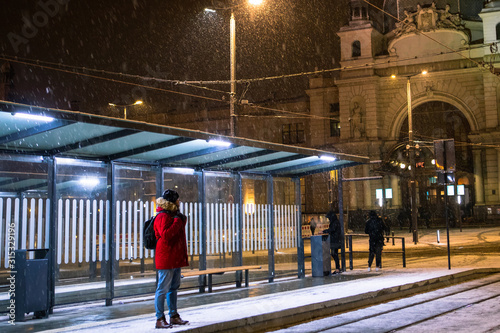 man at winter snowed night at railway station waiting for tram