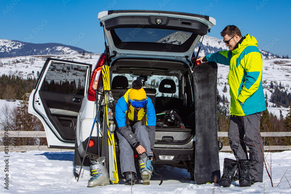 Fototapeta premium man and woman dressing into ski equipment near suv car