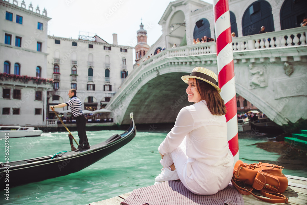 woman sitting near rialto bridge in venice italy looking at grand canal with gondolas