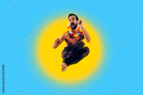 man with Hawaiian flower necklace jumping for joy against a blue sky and big sun background - vacations dreaming concept