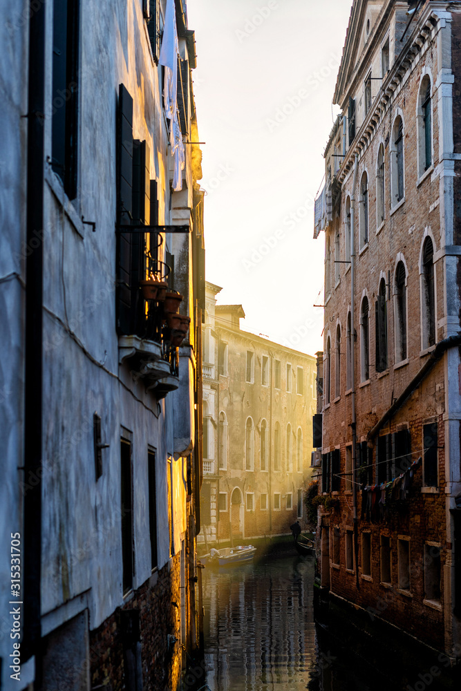 Classical picture of the venetian canals with gondola across the canal in beautiful evening light.