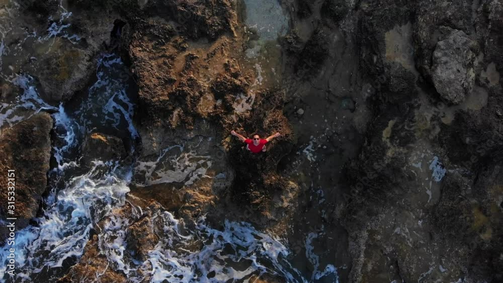 Camera quickly fly up, away from man standing on stony beach. Shallow waves splash around, dronie shot of tourist guy. Quad copter launch at sea shore Camera quickly fly up, away from man standing on stony beach. Shallow waves splash around, dronie shot of tourist guy. Quad copter launch at sea shore