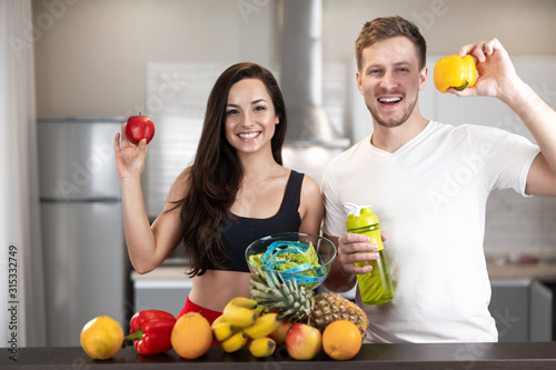 Photos young fit couple man and woman standing in the kitchen full of fruits and vegeta
