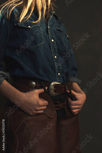 Blonde cowgirl with brown leather chaps and jeans shirt.