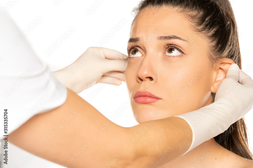 doctor's hands in gloves checks the ears of young woman