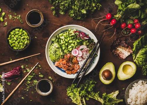 Healthy lunch, dinner. Flat-lay of salmon poke bowl or sushi bowl with vegetables, greens, sushi rice, soy sauce over rusty table background, top view. Traditional Hawaiian cuisine, clean eating food photo