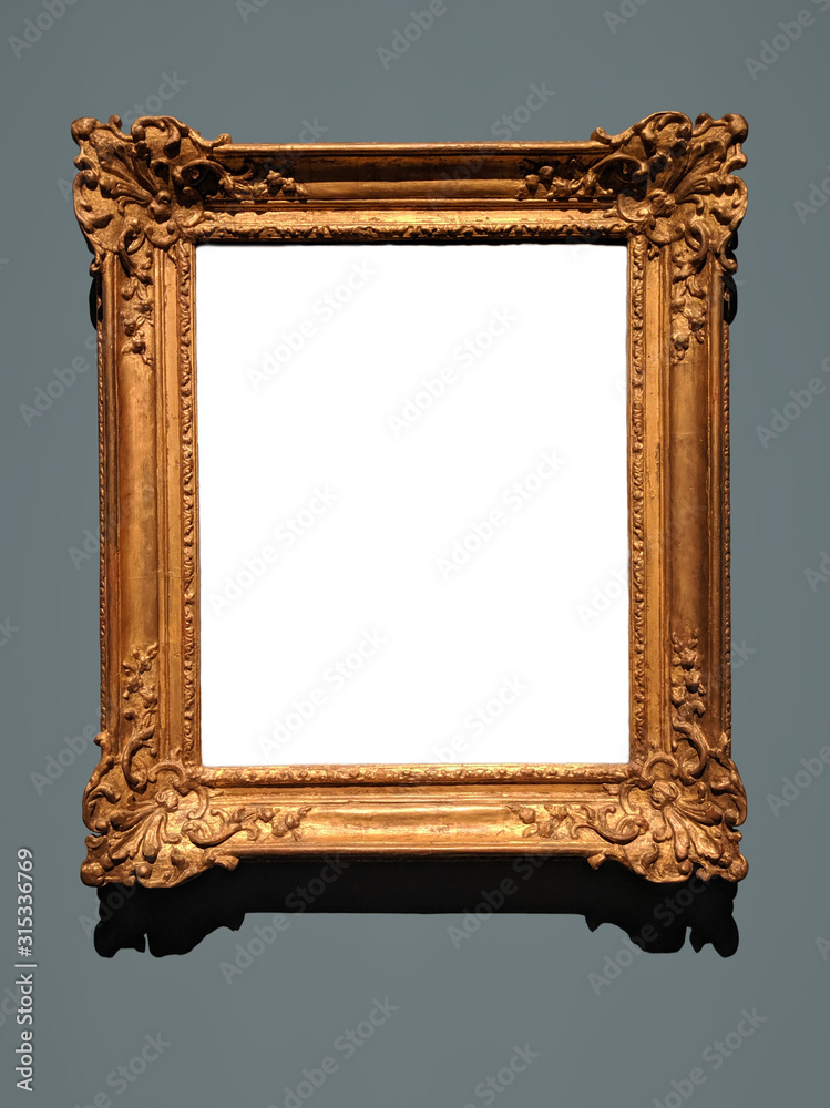 Blank canvas inside an elaborate golden wooden frame on a gray wall. Shadow  on top of white canvas and below the frame matches the lighting. Stock  Photo