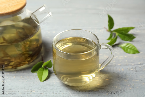 Cup of green tea, pot and leaves on grey wooden table