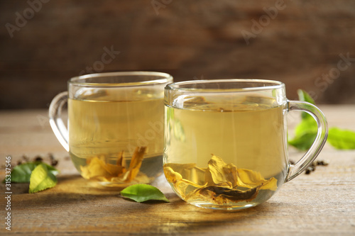 Cups of green tea and leaves on wooden table