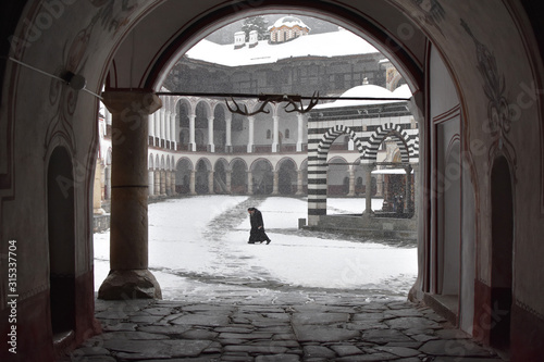 Snowy winter day in Rila Monastery, Bulgaria. Two monks crossing snow covered monastery yard