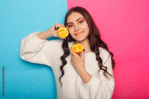 Funny young girl in summer clothes covering eyes with halfs of fresh ripe grapefruit orange fruit isolated on pink pastel background. People vivid lifestyle relax vacation concept. Mock up copy space