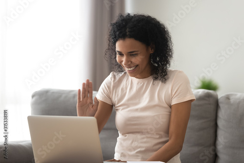 Woman sitting on couch looking at computer screen wave hand