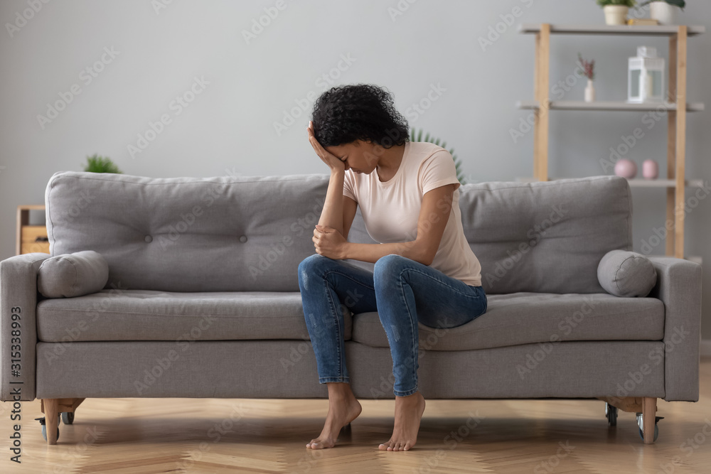 African female crying feels unhappy sitting on couch at home African female crying feels unhappy sitting on couch at home