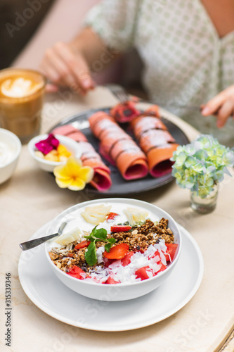 Sweet  vegan and healthy breakfast at Bali cafe. Bowl of homemade granola with yogurt and fresh berries on marble table.