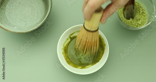 Blending green matcha tea powder in hot water with bamboo whisk to make green matcha tea latte