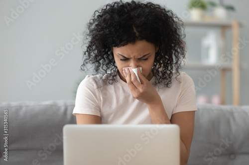 African woman holding handkerchief blowing runny nose working on laptop photo