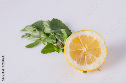 Half of juicy lemon with mint leaves. Fresh sour fruit with herb on white background.
