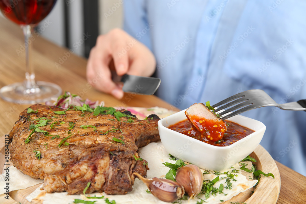 Woman eating delicious grilled pork chop at wooden table, closeup