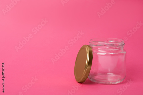 Open empty glass jar on pink background, space for text