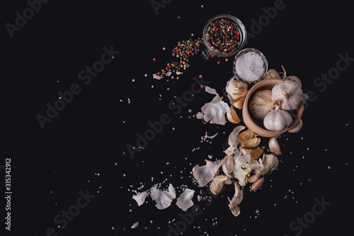 Garlic cloves on black surface. Mix of allspice and clove. Slt in glass cup. Black studio. photo