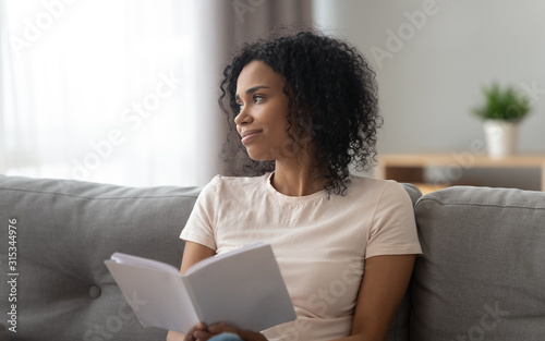 African woman distracted from reading looks out the window