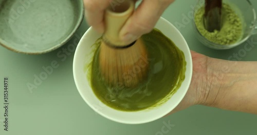 Blending green matcha tea powder in hot water with bamboo whisk to make green matcha tea latte